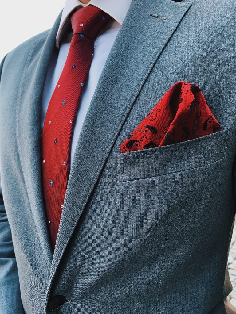 Szary garnitur z dodatkami: czerwony krawat oraz czerwona poszetka. Jak ubrać się na wesele? 